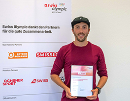 Marc Gürber steht vor einem Panel mit den Partner und Sponsoren von Swiss Olympic und hält die Urkunde für den 3. Platz der Swiss Olympic Science Awards in den Händen.