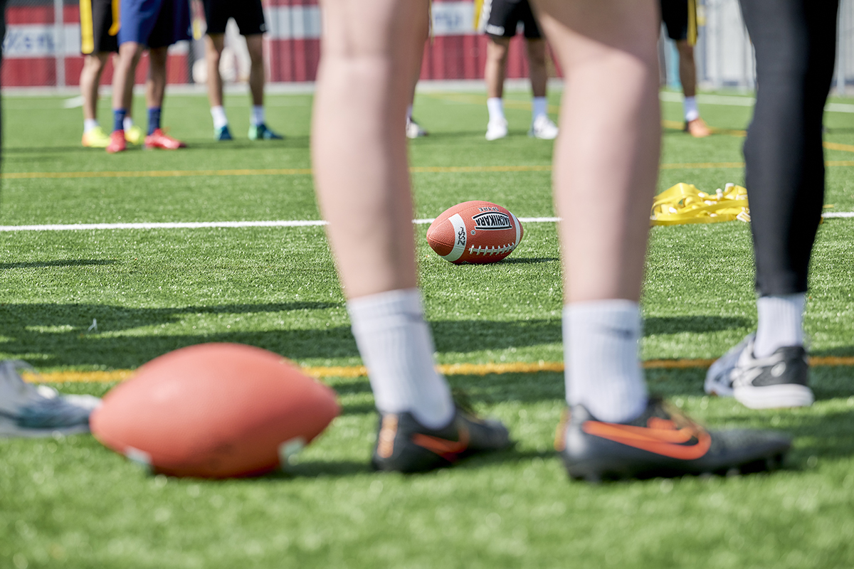 Ein Rugbyball liegt zwischen Beinen auf dem Rasen.